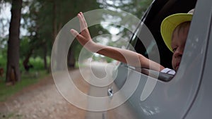 boy in hat waves from traveling car outside city. Traveling by car. Freedom, vacation. pleasure of relaxation. long trip