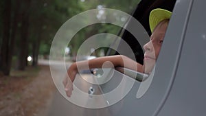 boy in hat waves from traveling car outside city. Traveling by car. Freedom, vacation. pleasure of relaxation. long trip