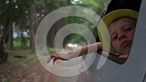 boy in hat waves from traveling car outside city. Traveling by car. Freedom, vacation. pleasure of relaxation. long trip