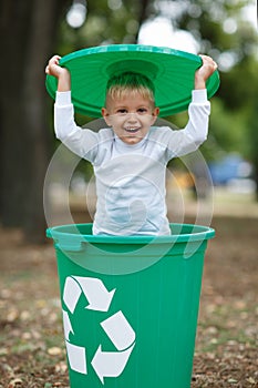 Boy have fun inside recyling waste bin outside. Concept of environmental protection. Colorful boxes.