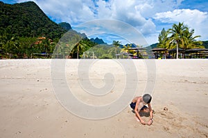 Boy having fun outdoors playing in the sand by the beach in tropical island