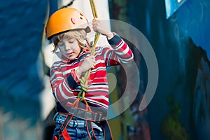 Boy having fun and playing at adventure park, holding ropes and climbing wooden stairs