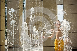 Boy having fun in water fountains. Child playing with a city fountain on hot summer day. Happy kids having fun in fountain. Summer