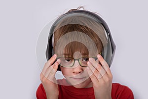 Boy in headphones corrects glasses. Portrait of child on white background, close up