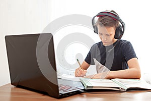 A boy in headphones in front of a computer does his homework. Distance learning in quarantine. Textbooks  are on the table