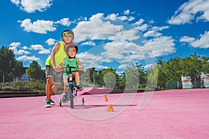 Boy help brother learn ride a bicycle going around orange cones