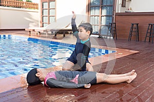 Boy helping drowning child girl in swimming pool by doing CPR.