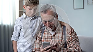 Boy helping grandfather to better understand smartphone, digital generation gap