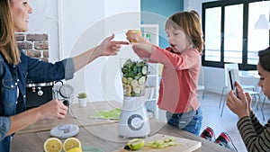 Boy helping his mother to prepare a detox juice with blender while his brother take photographs.