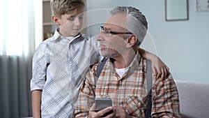 Boy helping old man to better understand smartphone, digital generation gap