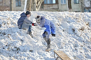 A boy helps a girl with a sled to climb a snowy hill