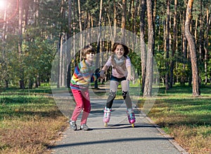 Boy helps the girl to roller-skate in the park. Brother supports