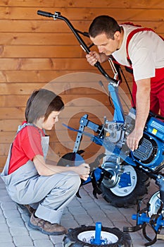 Boy helps his father mounting a cultivator machine photo