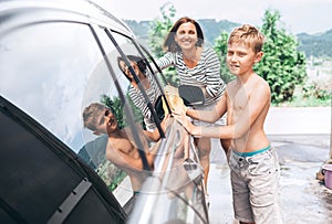 Boy helps his mother to wash a car