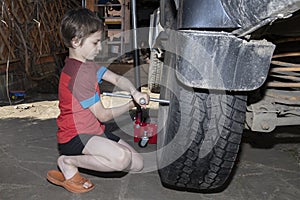 Boy helps to change the wheel of the car. Child works in the backyard of a house near the garage, sunny summer day. Side view