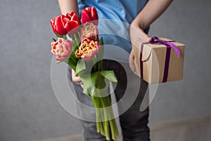 The boy hides a bouquet of flowers and a box with a gift for his mother behind his back