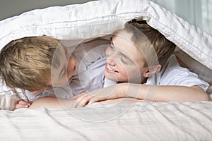 Boy hiding in bed under a white blanket or coverlet.