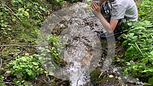 A boy hiker, trekker getting clear fresh water from a mountain spring in metal tourist cup and drinking