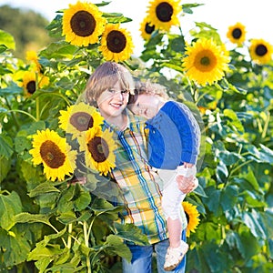 Boy with his baby sister in sunflower field at sunset