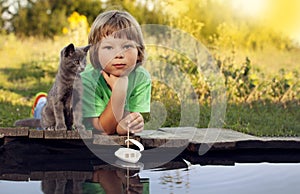 Boy and his beloved kitten playing with a boat from pier in pond