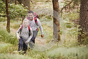 A boy and his father walking together on a trail between trees in a forest, both smiling, elevated view