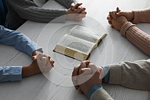 Boy and his godparents praying together at white wooden table, closeup