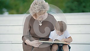 A boy with his grandmother reading and sitting on the white steps in the park