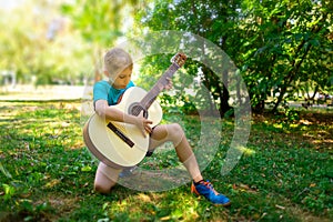 A boy in his hands with a guitar in the park tunes it, but looks at the strings