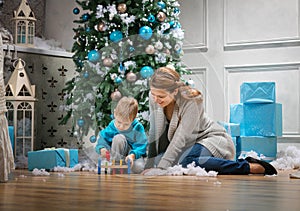 Boy and his mom playing with wooden hammer toy while sitting beside Christmas tree