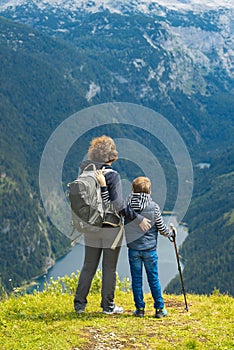 The boy and his mother with backpacks are standing on the top of the mountain