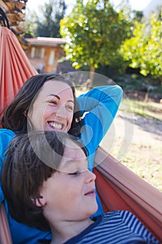 A boy with his mother are lying in a hammock in the courtyard of the house