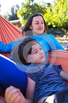 A boy with his mother are lying in a hammock in the courtyard of the house