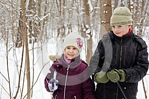 Boy and his sister stand in winter park with ski poles