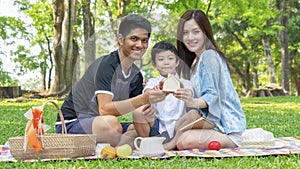 Boy hold money saving house box with mother and father in park.Happy family picnic concept