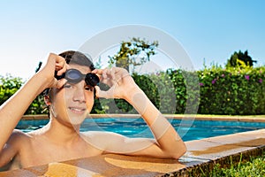 Boy hold swim googles on the border of a pool