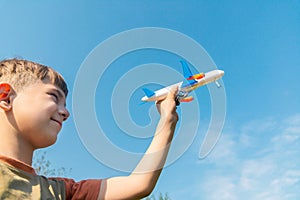 The boy is holding an airplane in his hand against the blue sky