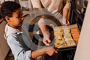 Boy holding baking sheet with vegetables while standing at the kitchen