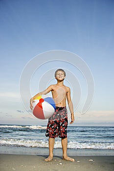 Boy holding beachball on beach.