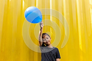 Boy holding blue balloons standing on yellow background.