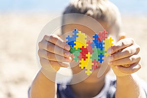 Boy holding colorful puzzle heart in front of his face. World autism awareness day concept