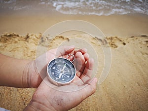 A boy holding a compass showing the direction point to north facing the ocean.