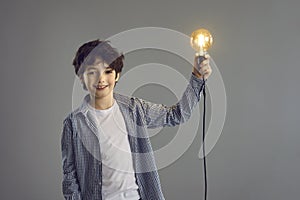 Boy holding glowing light bulb lamp standing isolated on grey studio copy space