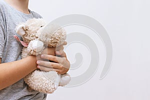 A boy holding, hugging a soft toy, teddy , white background, copy space