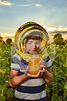 A boy holding a jar of honey in his hands on a field among sunflowers, the concept of an apiary
