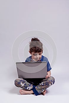 Boy holding a laptop while sited in the floor