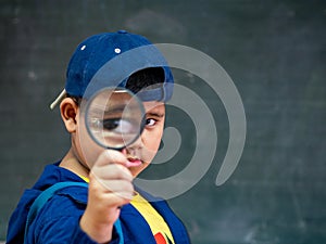 The boy holding the magnifying glass in front of blackboard. Back to School, Education Concept.