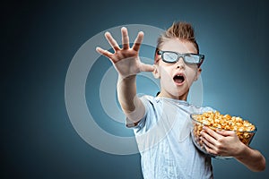 A boy holding popcorn in his hands watching a movie in 3D glasses, fear, blue background. The concept of a cinema, films, emotions