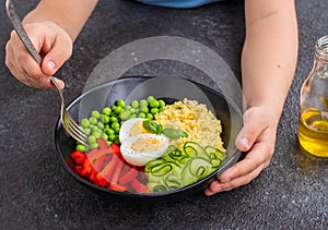 The boy is holding a salad bowl with green peas, millet, sweet pepper, fresh cucumber and boiled egg