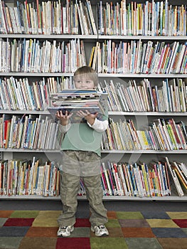Boy Holding Stack Of Books In Library