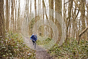 Boy holding stick running through a wood followed by pet dog